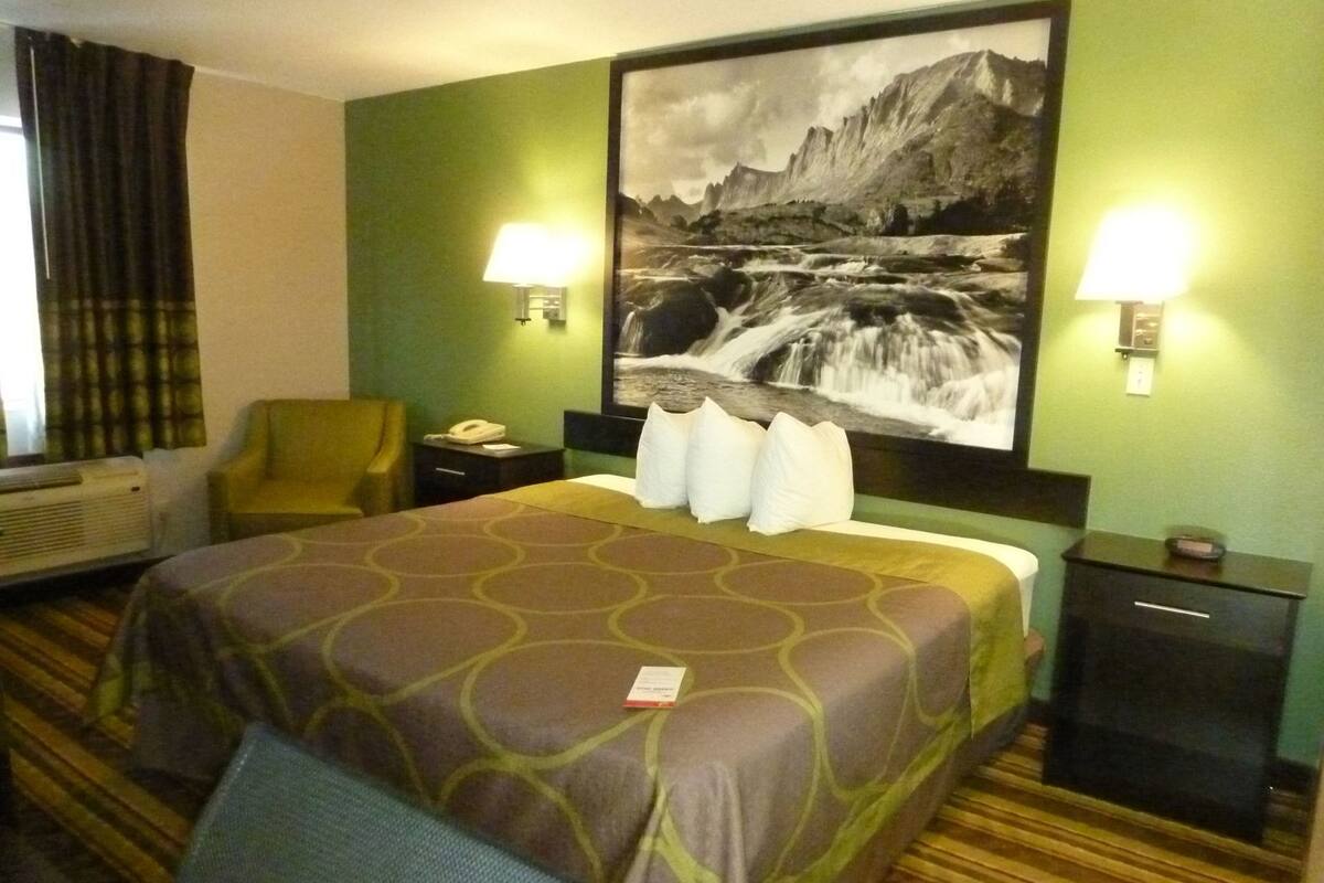 Een hotelkamer met een bed, een stoel, een bureau, een lamp en een schilderij aan de muur.