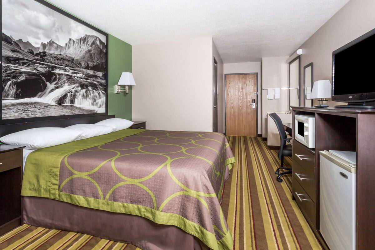 Een hotelkamer met een groot bed, een bureau met een computer, een televisie en een badkamers deur.