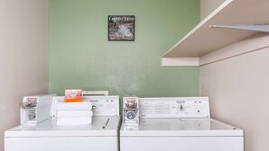 Een wasserette met twee wasmachines, een bord met wasregels aan de muur, en een plank boven de machines.