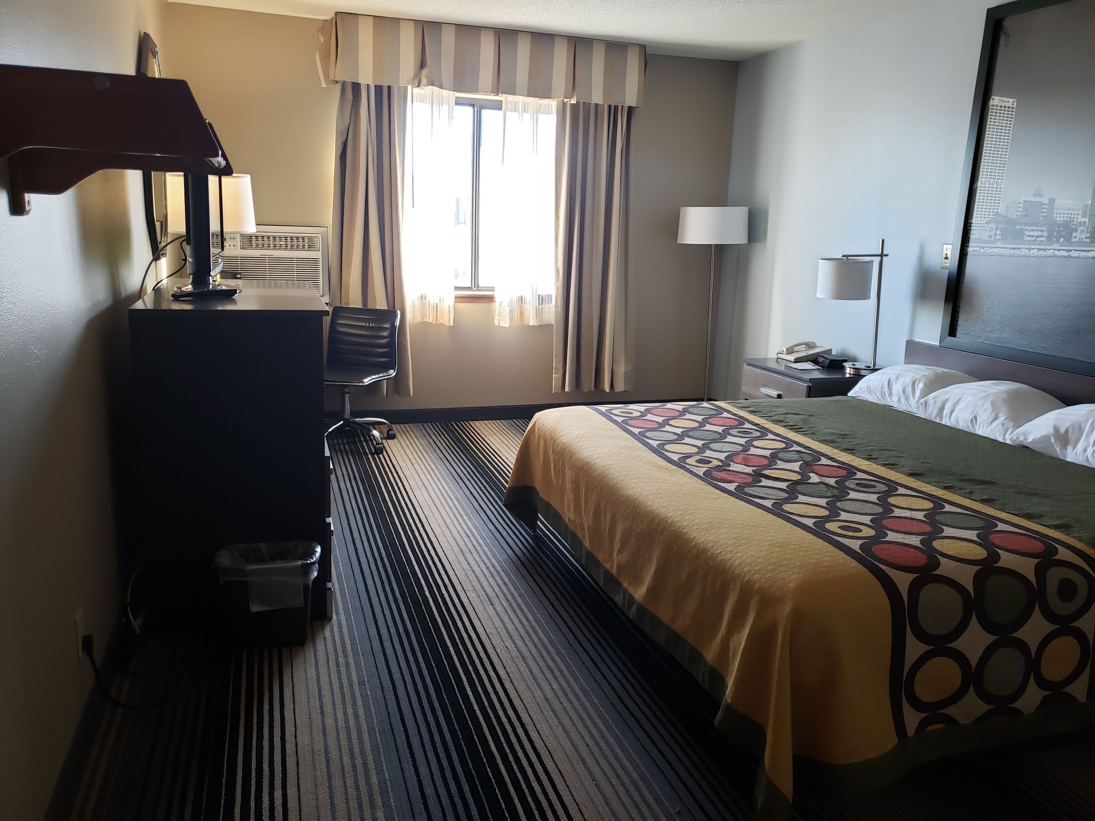Une chambre d’hôtel équipée d’un lit, d’un bureau, d’une chaise, d’une lampe et offrant une vue sur le paysage urbain par la fenêtre.