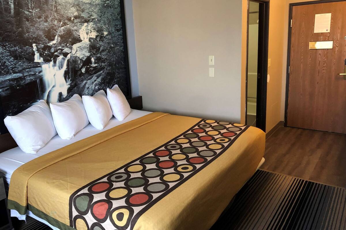 A hotel room with a bed, a large painting of a waterfall, and a wooden door.