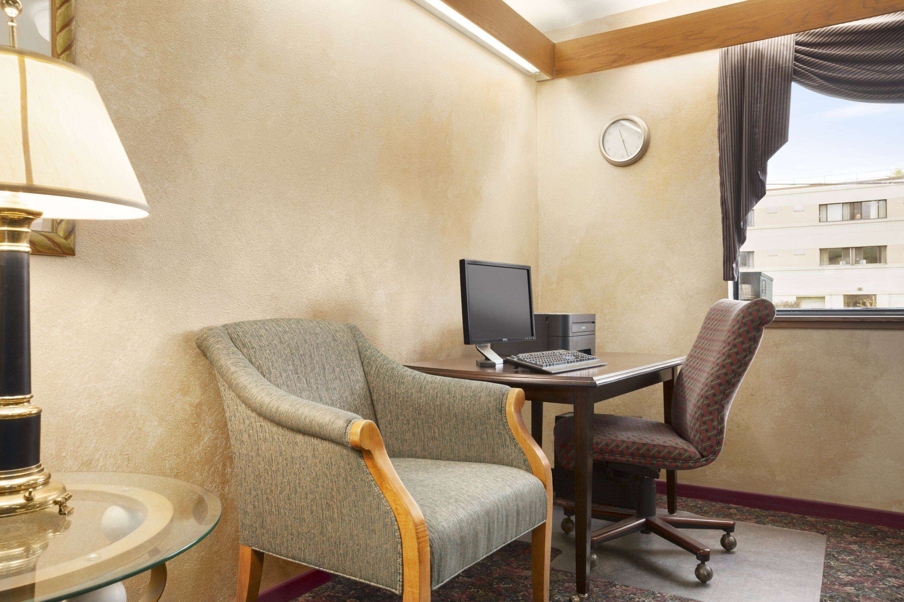 Ein Hotelzimmer mit Schreibtisch, zwei Stühlen, einem Computer, einer Lampe und einer Wanduhr.