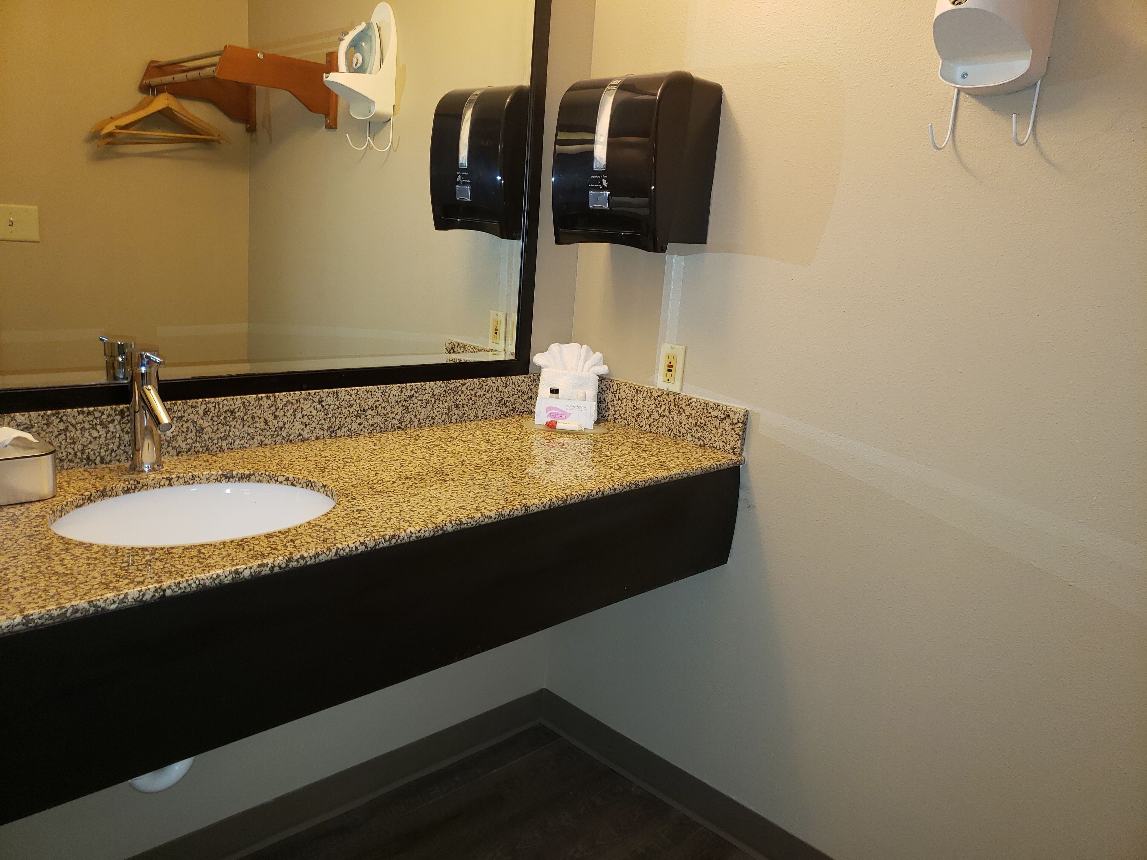 A bathroom with a granite countertop sink, a mirror, a towel dispenser, and a hand dryer.