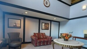 Un vestíbulo amplio con un sofá rojo, una mesa redonda con un jarrón de flores y un reloj en la pared.