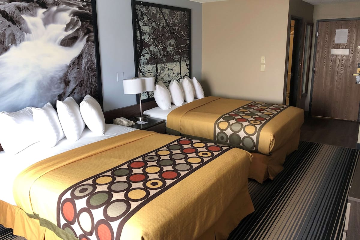A hotel room with two beds, a large mural on the wall, a lamp, and a door with a sign.