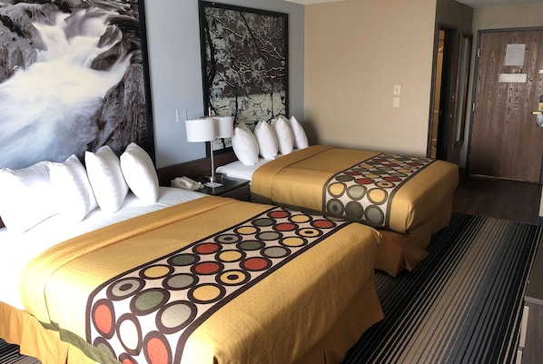 A hotel room with two beds, a large mural on the wall, a lamp, and a door with a sign.