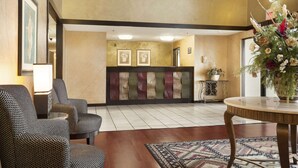 Un hall de hotel con sillas estampadas, un mostrador de recepción y un jarrón decorativo.