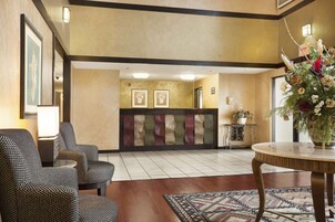 Un hall de hotel con sillas estampadas, un mostrador de recepción y un jarrón decorativo.