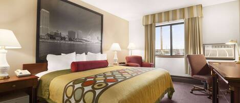 Habitación de hotel con una cama grande, dos mesitas de noche con lámparas, un escritorio con una silla, un ventanal con cortinas y un cuadro de paisaje urbano en la pared.