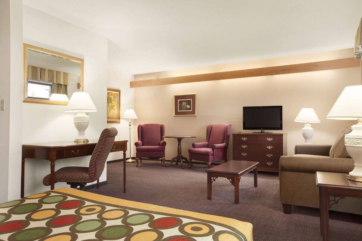 A hotel room with a bed, two armchairs, a sofa, a TV, a desk, and a dresser.