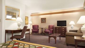 Een hotelkamer met een bed, twee fauteuils, een bank, een televisie, een bureau en een dressoir.