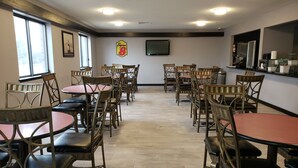 Un comedor con mesas y sillas redondas, un televisor montado en la pared y el logotipo de Super 8.