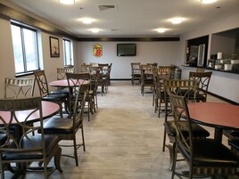 Un comedor con mesas y sillas redondas, un televisor montado en la pared y el logotipo de Super 8.