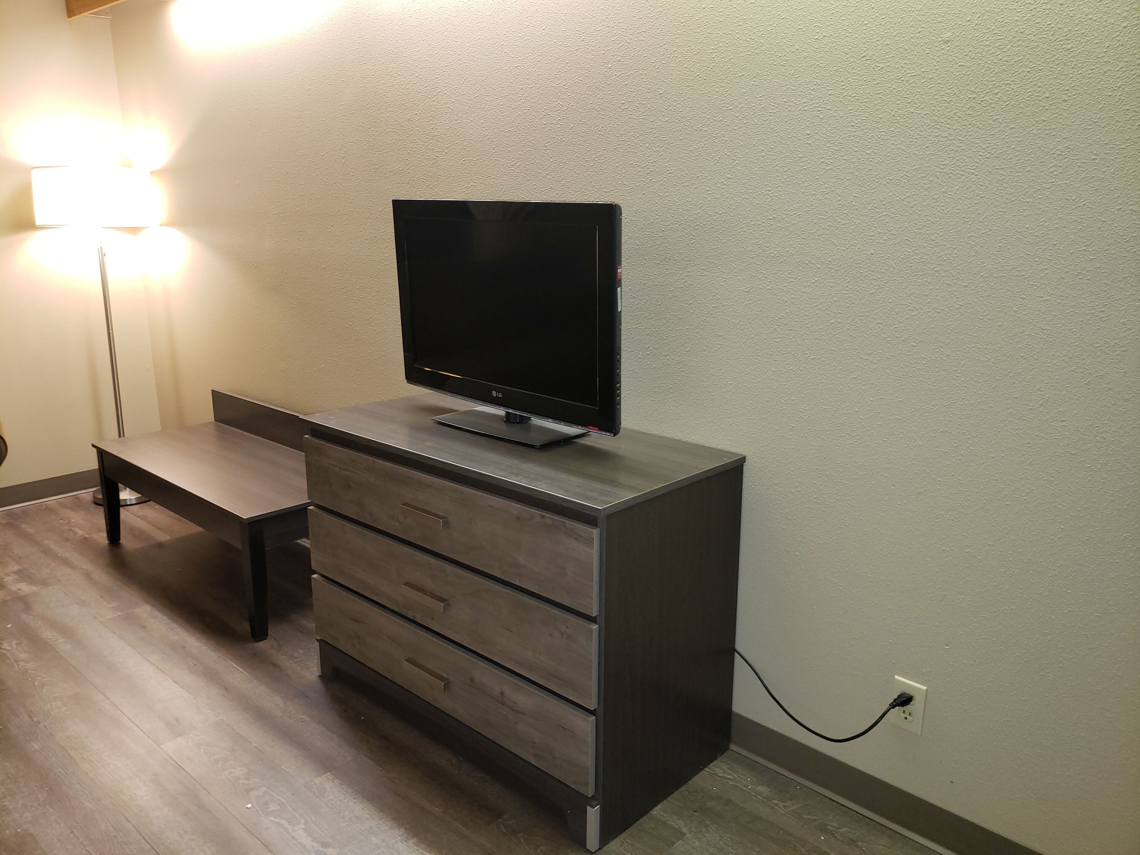 A modern room with a flat-screen TV on a wooden cabinet, a floor lamp, and a power outlet on the wall.