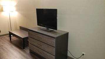 A modern room with a flat-screen TV on a wooden cabinet, a floor lamp, and a power outlet on the wall.