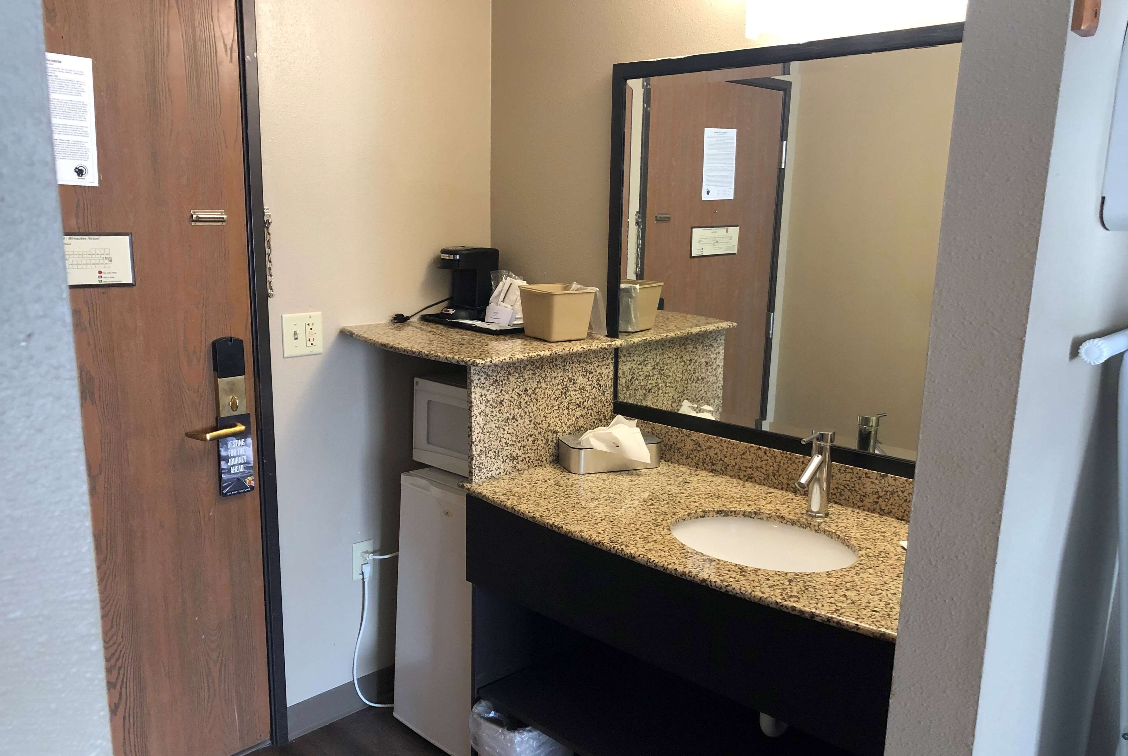Baño compacto con encimera de granito, lavamanos, espejo, cafetera y cesto de basura.