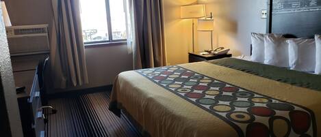 Una habitación de hotel con cama, lámpara de noche, teléfono y ventana con cortinas.