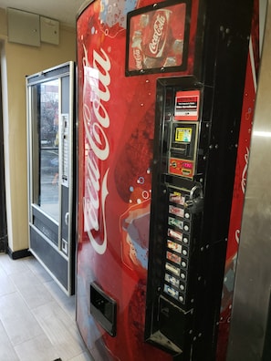A Coca-Cola vending machine with a selection of beverages and a warning sign about property surveillance.