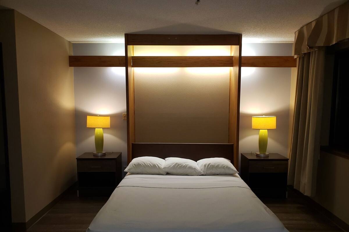 A hotel room with a large bed, two bedside tables with lamps, and a wooden headboard.