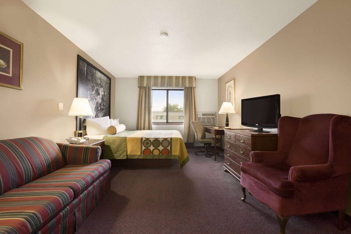 A hotel room with a bed, a sofa, a desk, a television, and a chair.