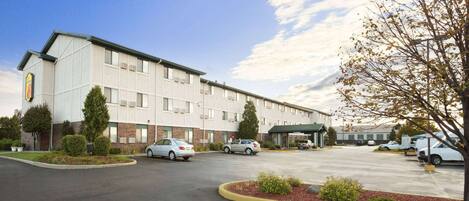 A hotel with a parking lot, multiple cars, and a building with a green roof.