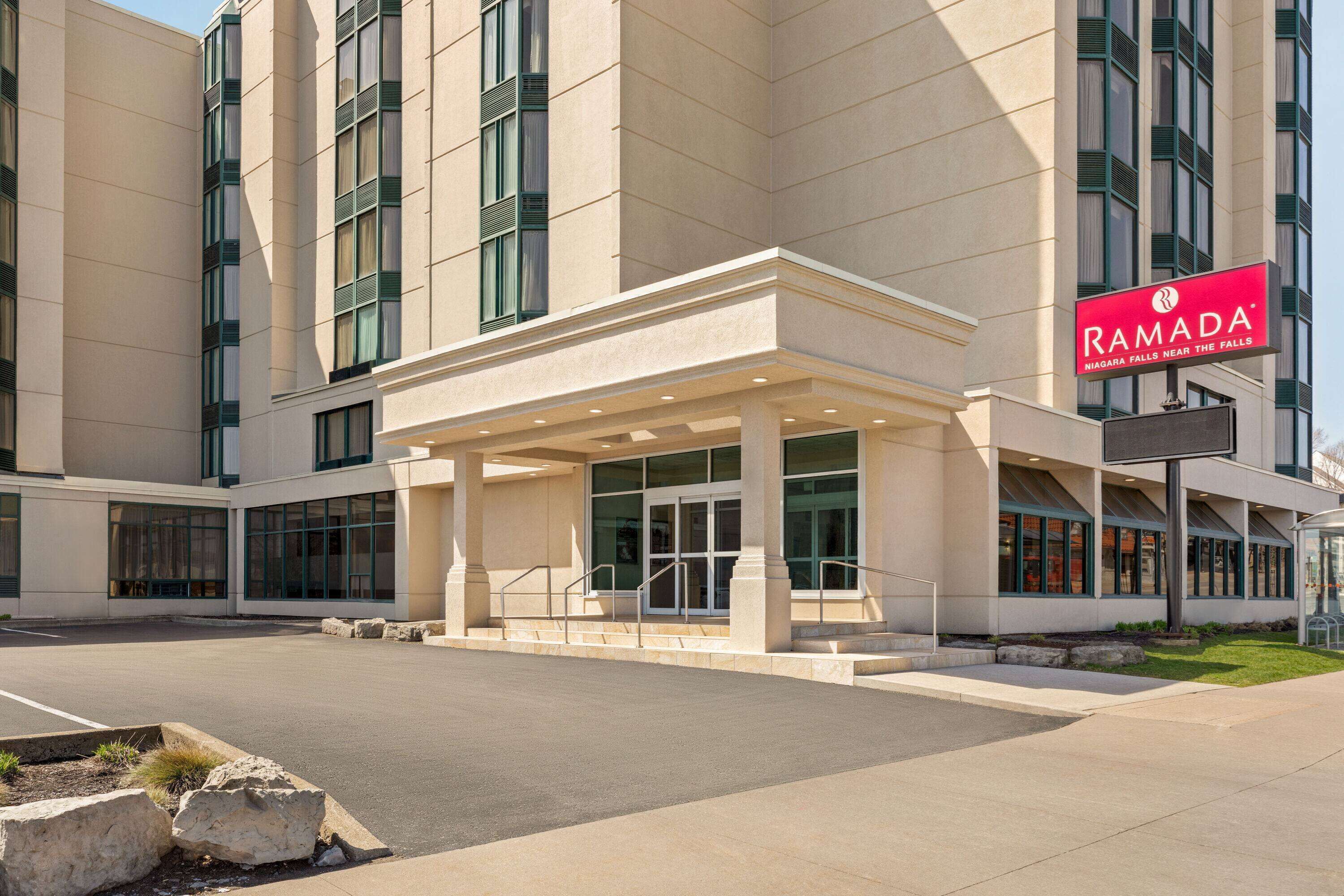 Een modern gebouw met een overdekte ingang, grote ramen en een bord met daarop Ramada Niagara Falls.