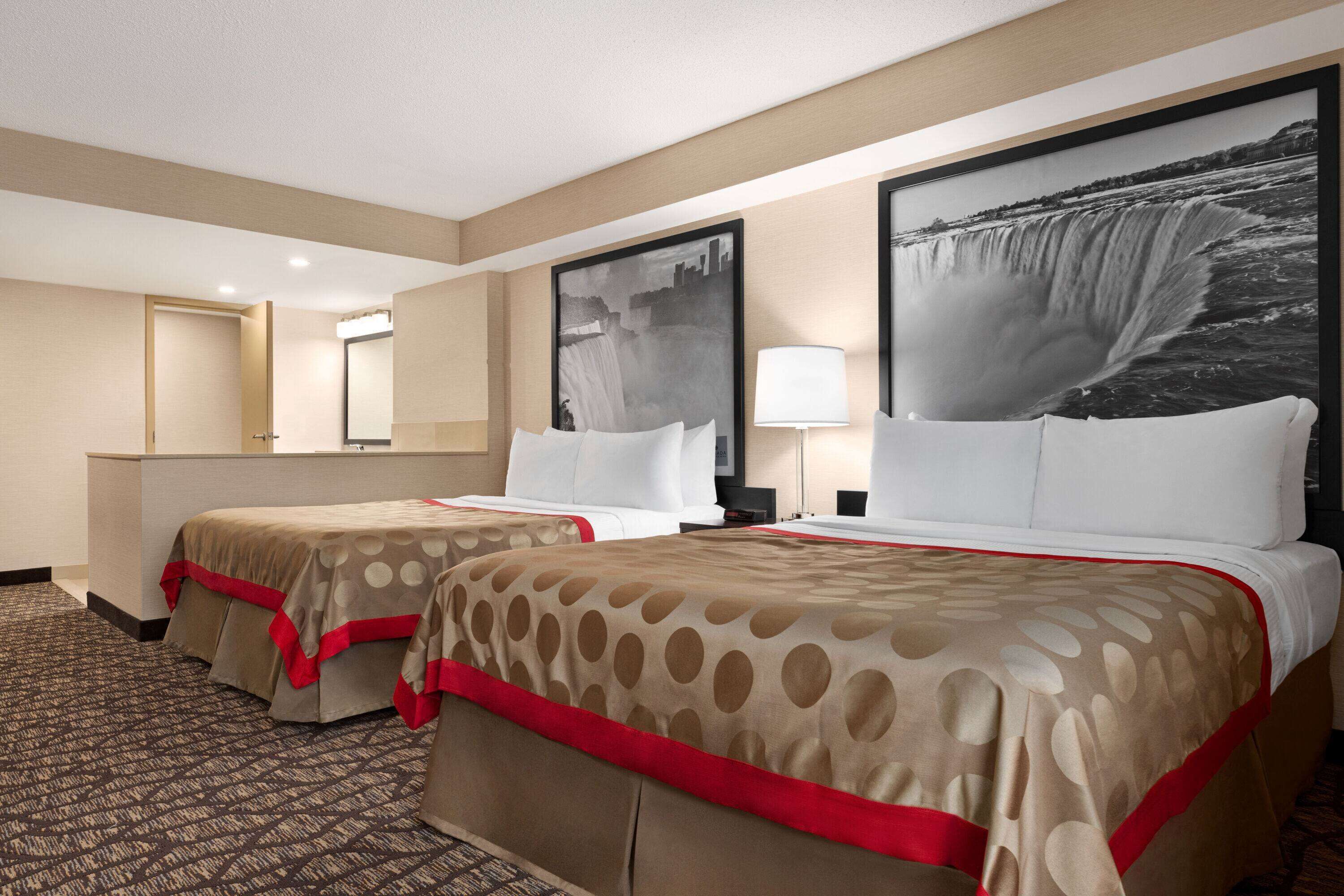 Una habitación de hotel con dos camas, un cuadro grande de una cascada en la pared y suelo alfombrado.