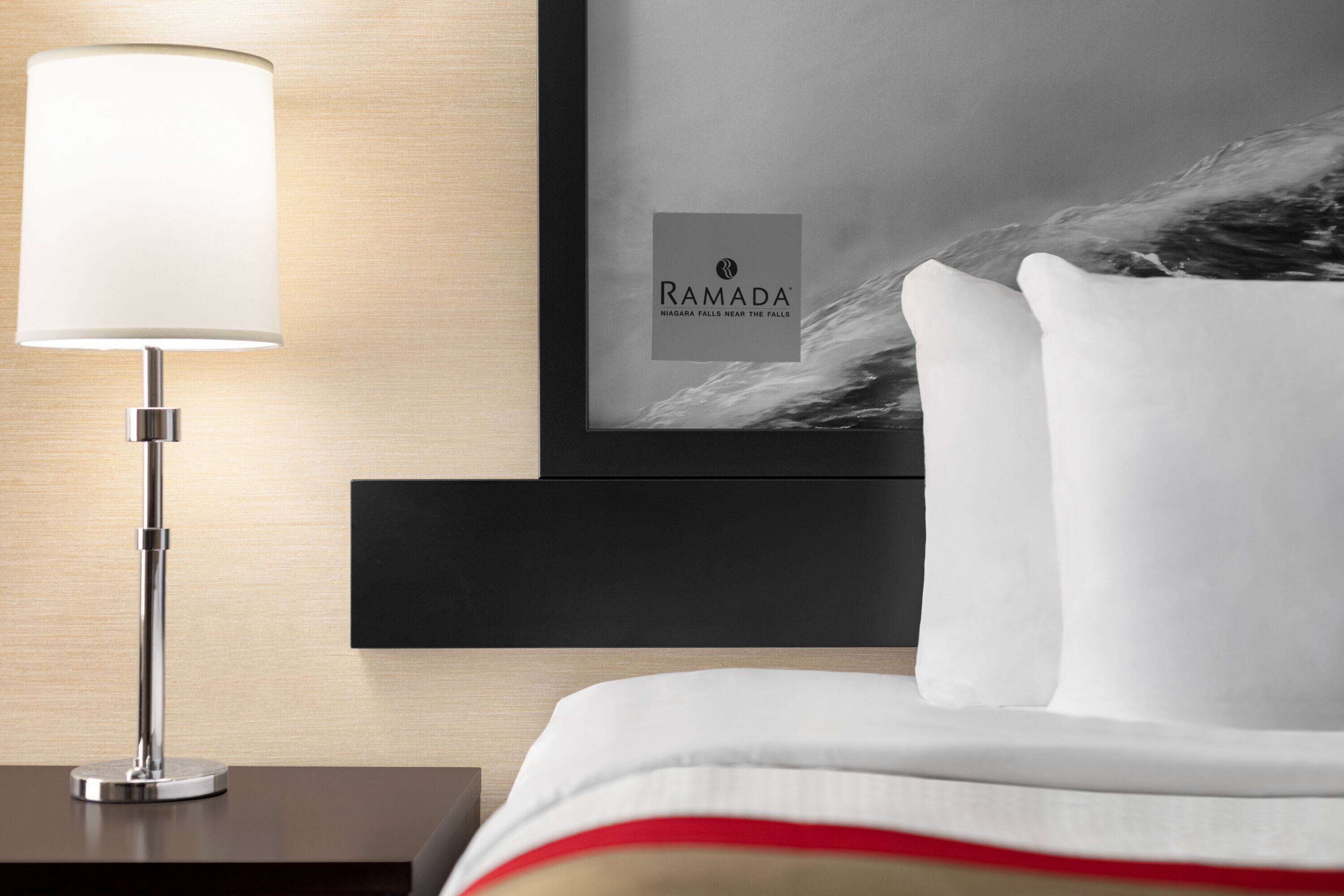 A hotel room with a framed picture of Niagara Falls, a modern lamp, and a neatly made bed.