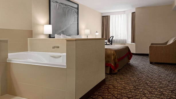 Habitación de hotel con bañera, cama con colcha roja, escritorio con lámpara y una silla.