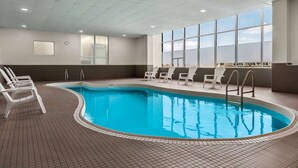 Piscina interior con agua azul cristalina, rodeada de sillas blancas y suelo de baldosas.