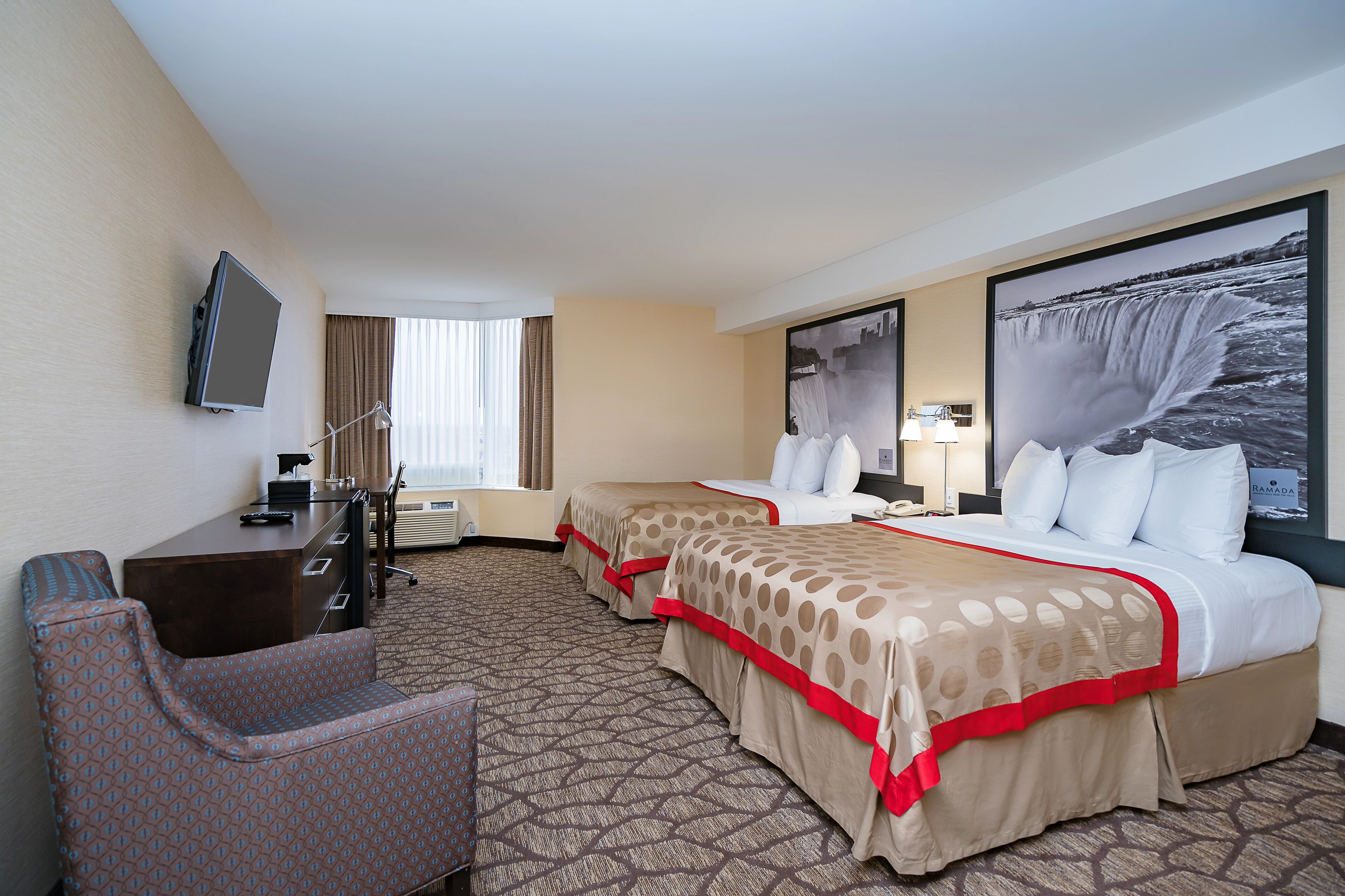 A hotel room with two beds, a desk, a chair, a TV, and a large window.