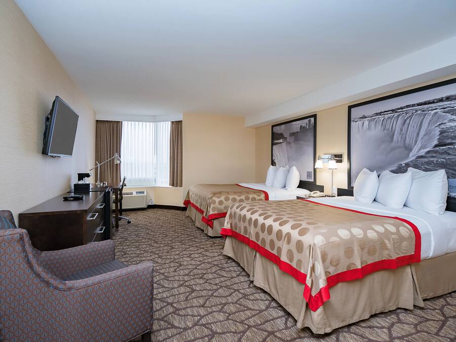 A hotel room with two beds, a desk, a chair, a TV, and a large window.