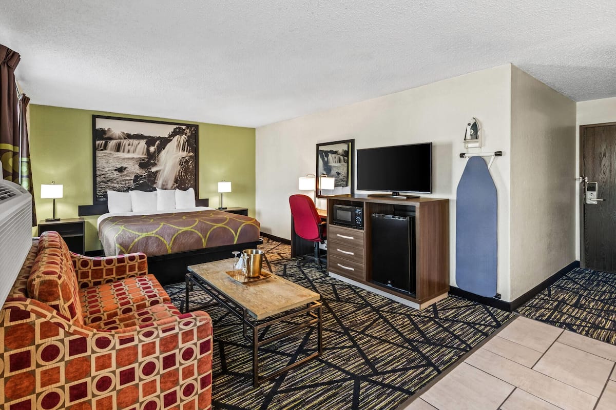 A hotel room with a bed, a sofa, a TV, a desk, and a kitchenette.