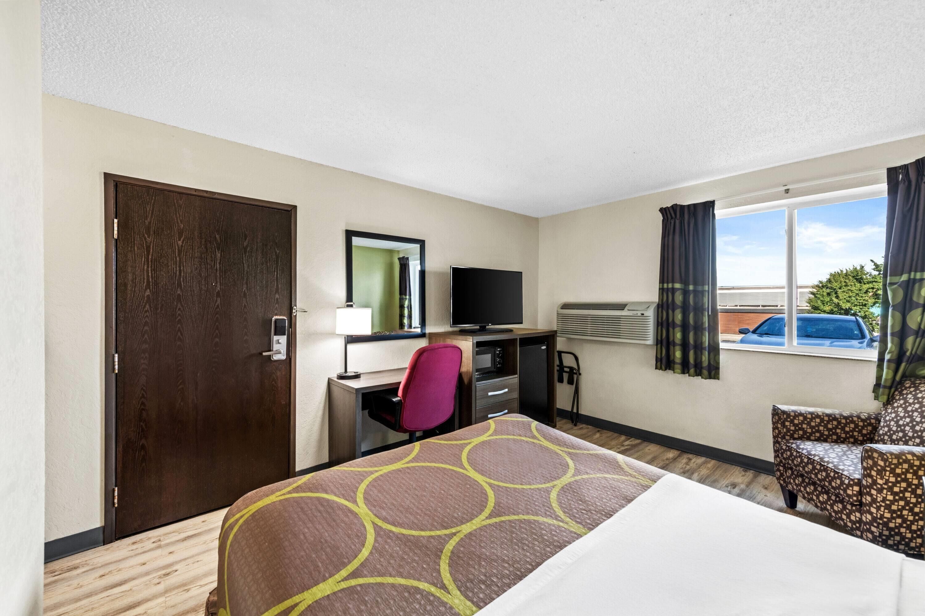 A hotel room with a bed, desk, chair, TV, and window with curtains.