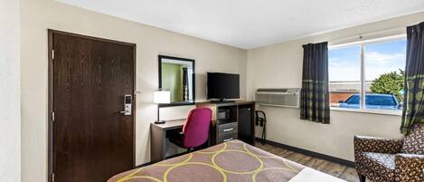 A hotel room with a bed, desk, chair, TV, and window with curtains.