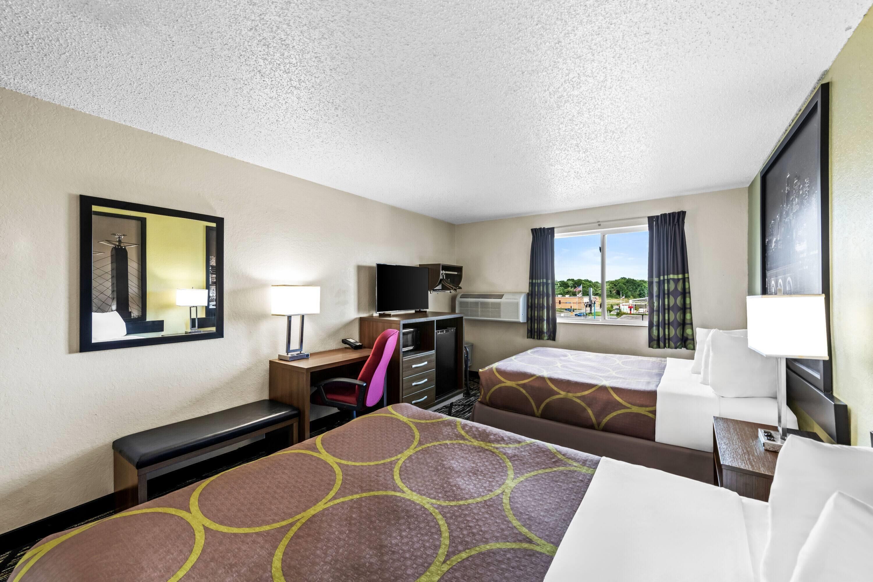 A hotel room with two beds, a desk with a chair, a TV, and a window with curtains.