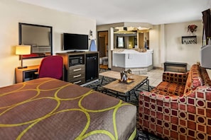 A hotel room with a bed, a desk with a computer, a TV, a sofa, and a bathroom visible through an open door. - Super 8 by Wyndham Independence Kansas City (Independence)