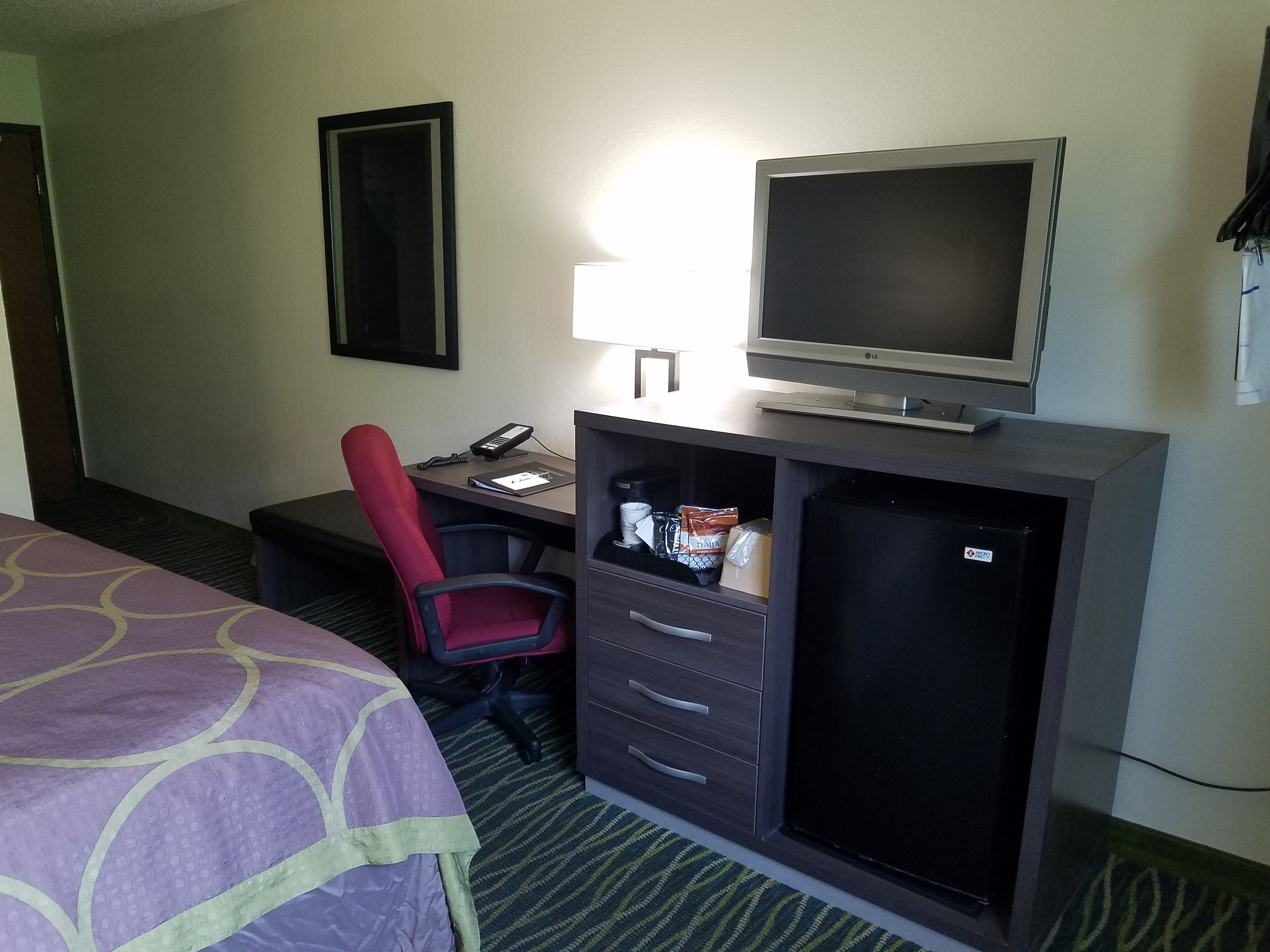 Una habitación de hotel con una cama, un escritorio con computadora y lámpara, una silla y un minibar.