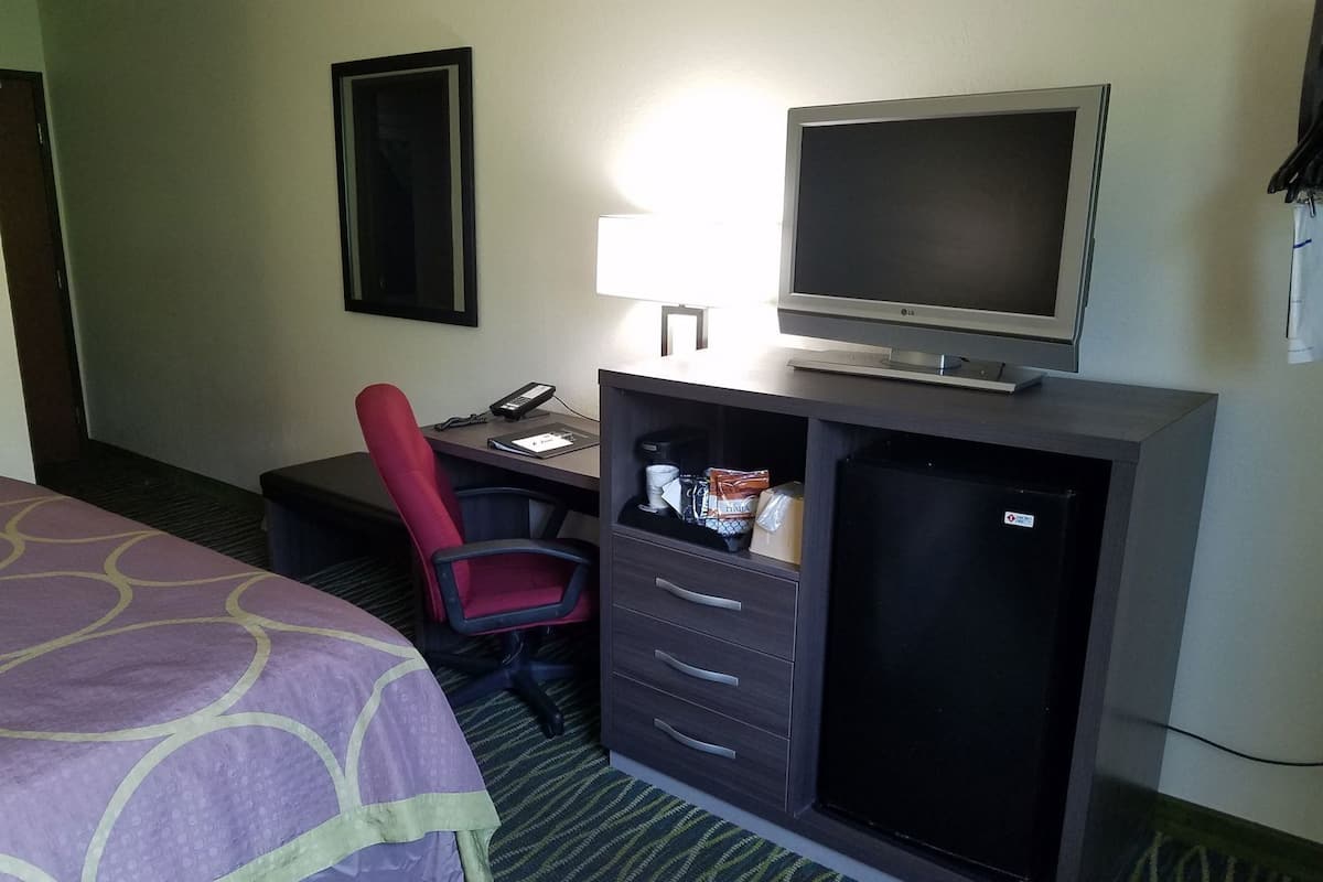 A hotel room with a bed, a desk with a computer, a chair, a TV, and a minibar.