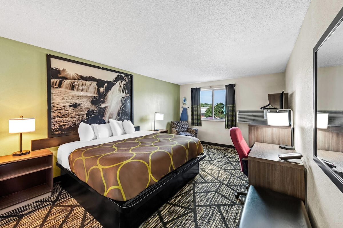 A hotel room with a large bed, a desk, a chair, a lamp, and a window with curtains.