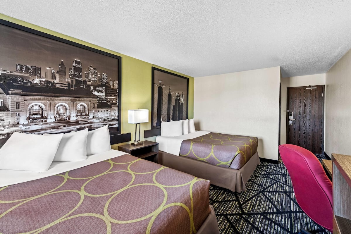 A hotel room with two beds, a desk, a chair, and a cityscape mural on the wall.
