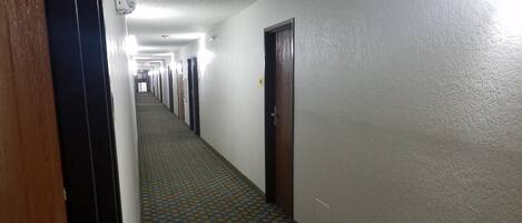 A long, narrow hallway with patterned carpet, doors on both sides, and a light fixture on the ceiling.