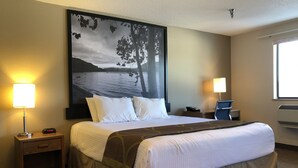 Habitación de hotel con una cama grande, dos lámparas de noche, un escritorio con una silla y un cuadro grande en la pared.
