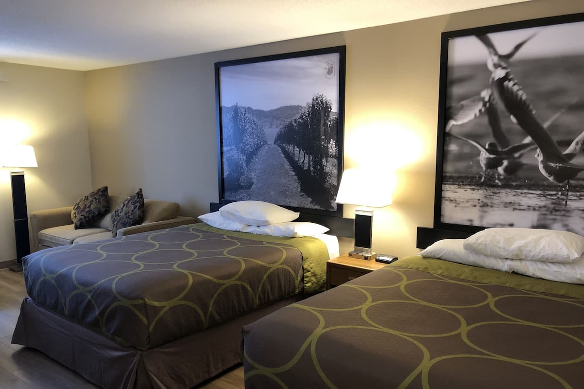 Habitación de hotel con dos camas, un sofá, una mesita de noche y una lámpara.