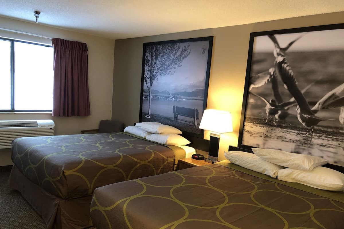 Habitación de hotel con dos camas, un ventanal amplio, un equipo de aire acondicionado y dos lámparas de pared.