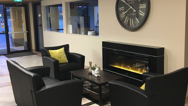 Un vestíbulo con un gran reloj de pared, sofás negros, una mesa de centro y una chimenea.