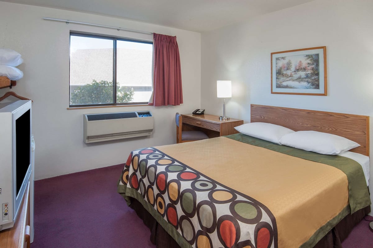Habitación de hotel con cama, escritorio, silla, ventana con cortinas, un cuadro en la pared y un equipo de aire acondicionado.
