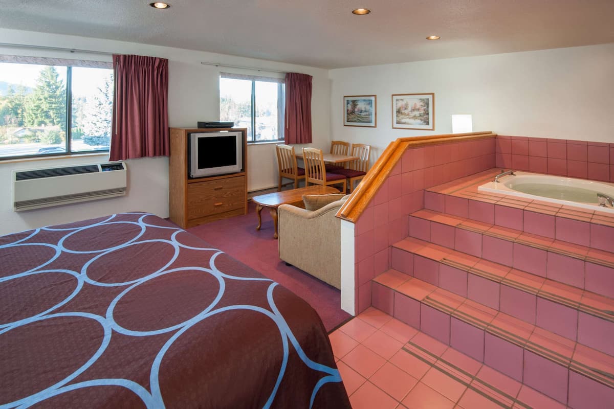 Habitación de hotel con cama, televisor, mesa de comedor con sillas, pequeña cocina y baño con bañera y escaleras.