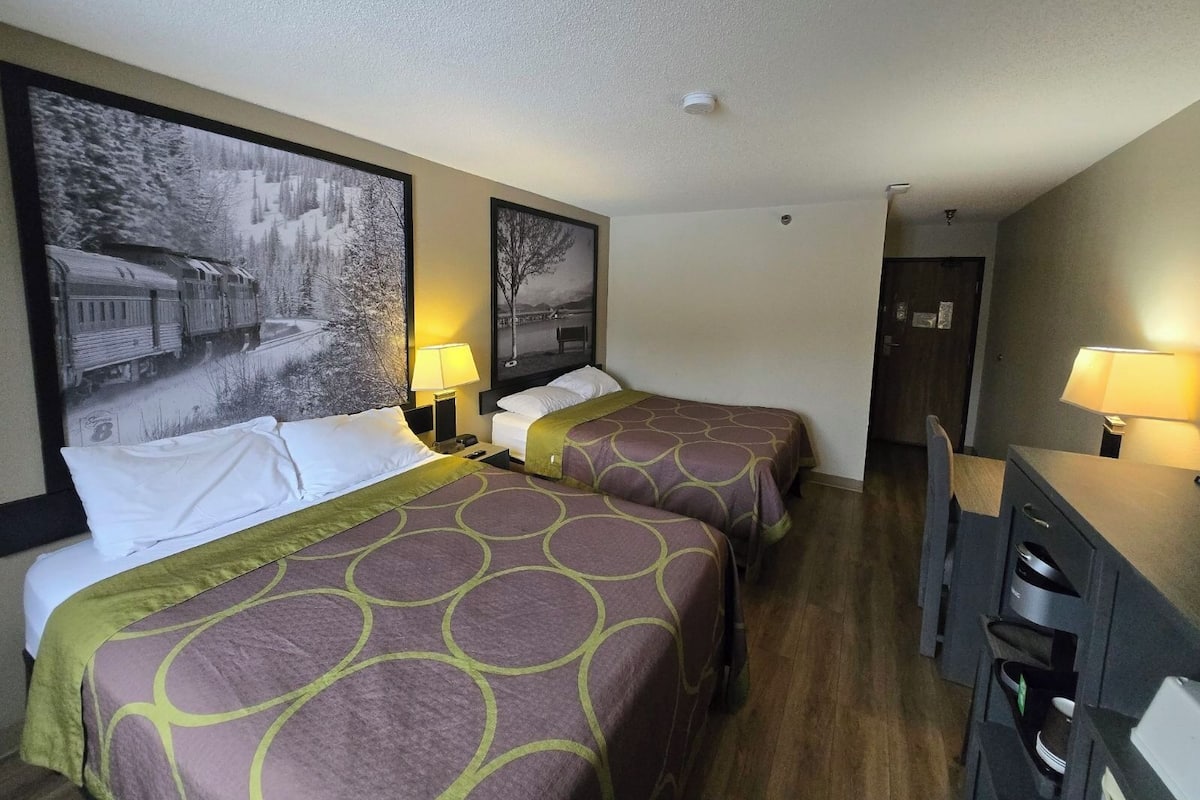 Habitación de hotel con dos camas, un escritorio y una silla. Cuenta con dos lámparas de pared y una luz de techo.