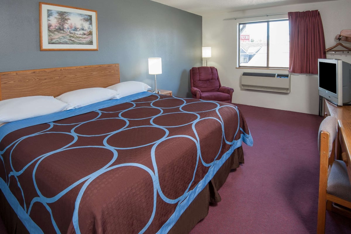 Habitación de hotel con una cama grande, una silla, un televisor y una ventana con cortinas.